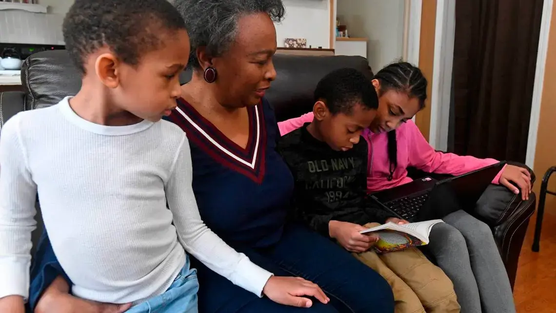 Regina Barrett, center, sits with her grandchildren Asa Barrett, left, 5, Hallie Barrett, 10, and Asher Barrett, 8, in her Monroe, NC home on Wednesday, February 10, 2021. Regina Barrett began juggling the roles of grandmother, caregiver and teacher to help out when the pandemic shutdown schools last year. Image by David T. Foster III. United States, 2021.