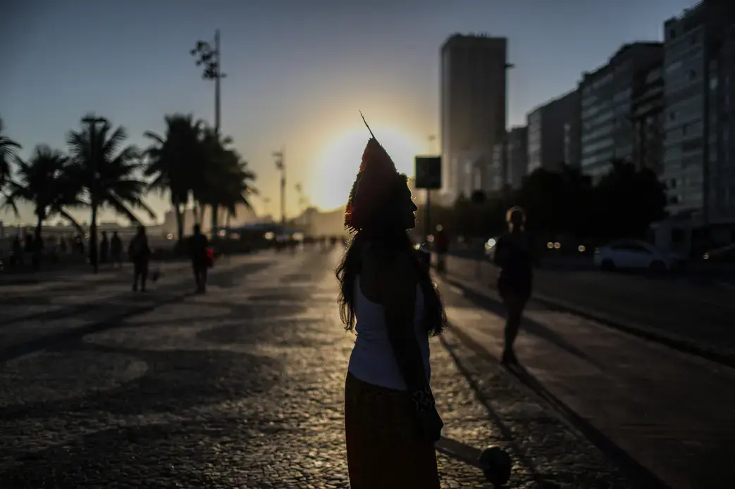 The silhouette of a woman in a headdress standing against the sun as it sets.