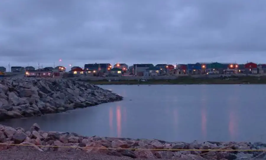 Buildings glow with lights in the distance, behind a body of water.