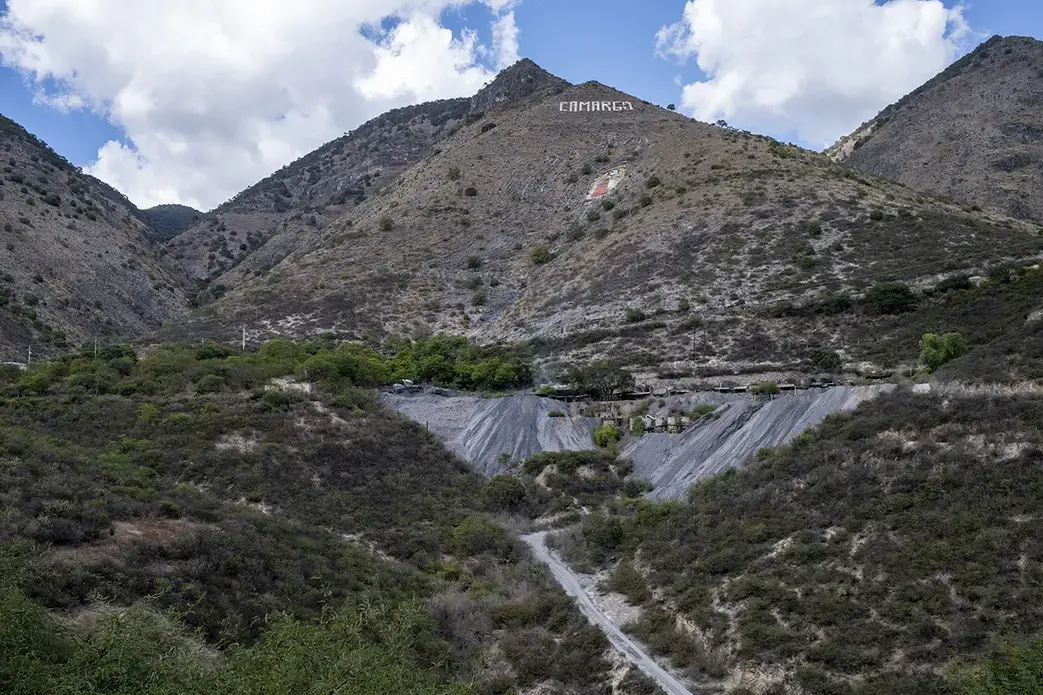 Una mina en la base de un paisaje montañoso. En la cima central está escrito "Carmago".