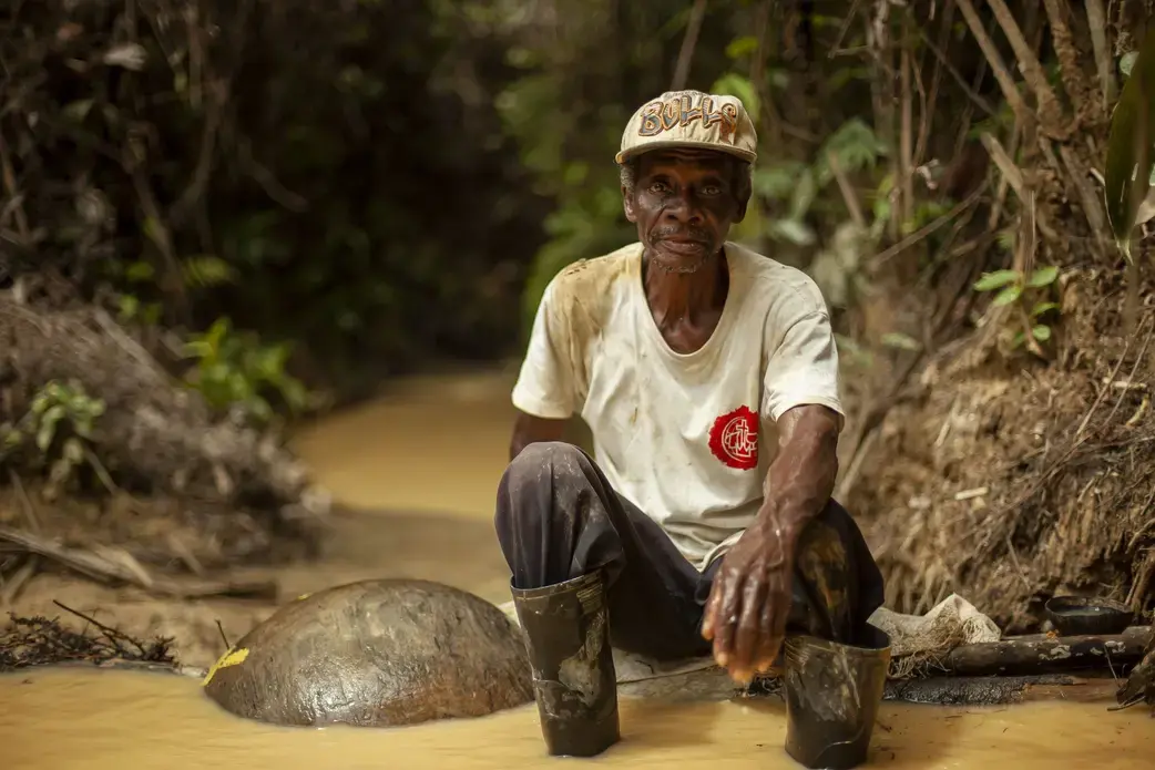 A man sits by the river where he pans for gold.