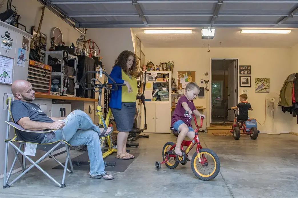 Elias and Crystal Camacho watch sons Elias, 4 (left), and Asher, 7, play in the garage of their Swannanoa home on June 30. Before finding a new day-care center for Elias after the one he was attending closed because of the COVID-19 pandemic, Camacho and her husband either took turns staying home half-days or taking the boys with them to work. Image by Angeli Wright/Asheville Citizen Times/North Carolina News Collaborative. United States, 2020.</p>
<p>