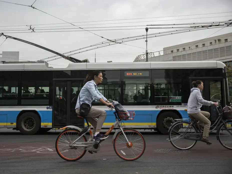 A woman rides a rental bike through an intersection on Wednesday, Sept. 27, 2017, in Beijing. Bikes and scooters have become a popular means of transportation in the large city where car traffic is always heavy. Image by Kelsey Kremer. China, 2017.