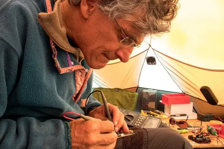 University of Wyoming glaciologist Neil Humphrey works on one of the tiny sensors the team sent down through a bore hole to collect information about the ice sheet bed. Image by Amy Martin. Greenland, 2018. 