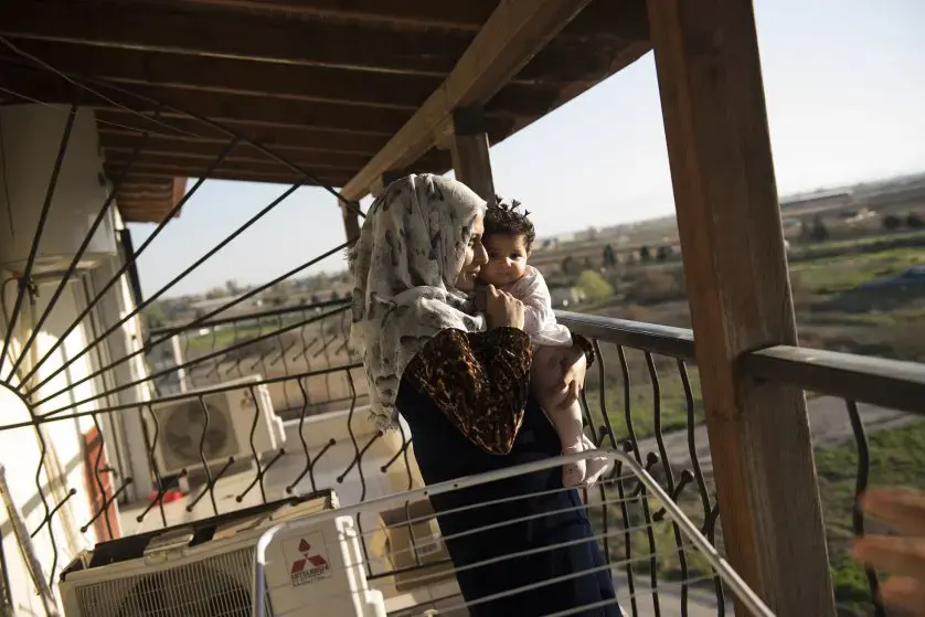 Noor Al Talaa, 22, stands on the balcony at dusk with baby Rahaf, almost 6 months, at an apartment in Sidros. Image by Lynsey Addario. Greece, 2017.