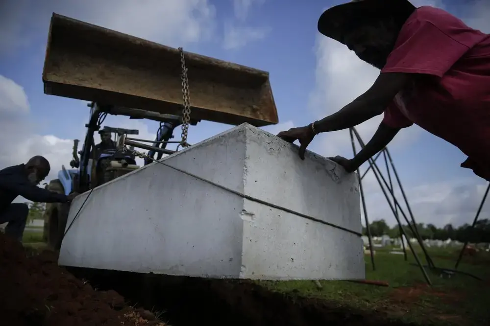Willie Johnson, 66, left, Horace Bell, 60, center, and Eugene Davis, 58, right, lower a burial vault into a grave at Cedar Hill Cemetery on Saturday, April 18, 2020, in Dawson, Ga. Image by Brynn Anderson / AP Photo. United States, 2020.