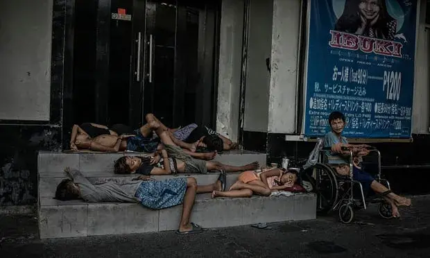 Street children and a man with cerebral palsy shelter in the doorway of a hostess bar in Malate, Manila, a known area for sex tourists from South Korea and Japan. In Manila, thousands of people sleep outside in doorways, under awnings on the sidewalks and on sea walls every night of the year. Image by James Whitlow Delano. Philippines, 2018. 