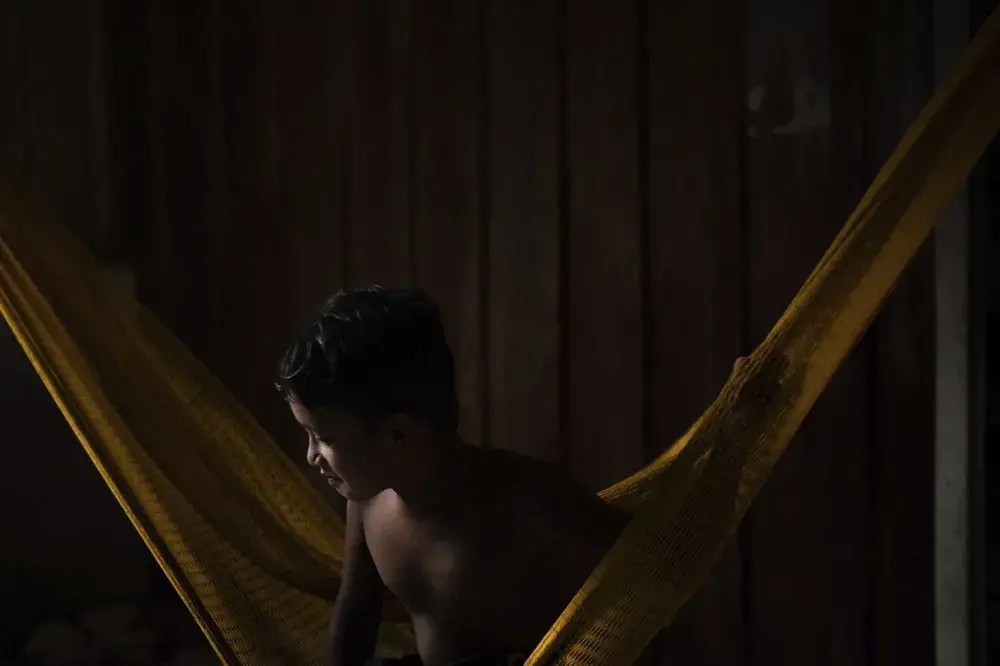 A youth from the Sateré Mawé indigenous ethnic group sits in a hammock in the Gaviao community near Manaus, Brazil, Friday, May 29, 2020. In the midst of the new coronavirus pandemic, Brazil's indigenous people have neither the protective isolation of their homelands nor the government care that drew many to the city of Manaus in the first place. Image by Felipe Dana / AP Photo. Brazil, 2020.