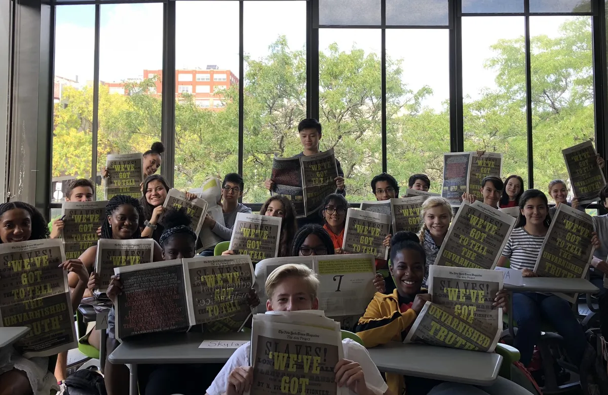 students in a classroom holding The 1619 Project