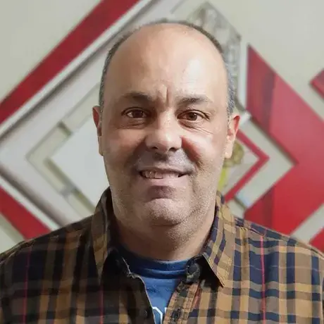 A man wearing a yellow stripe flannel shirt smiles at the camera.