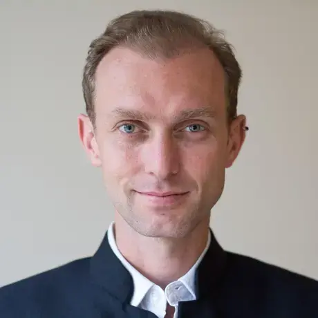 Sébastien Farcis A man wearing a white shirt and dark blue jacket. He has an ear piercing.