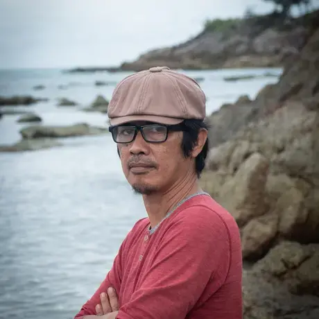 A person wears glasses, a brown baseball cap, and a red shirt.