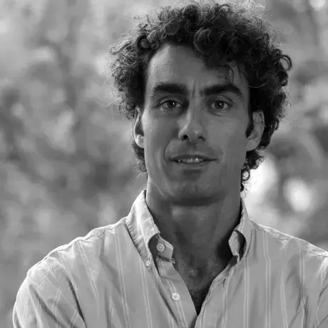 A man with curly hair and wears a white shirt smiles at the camera.