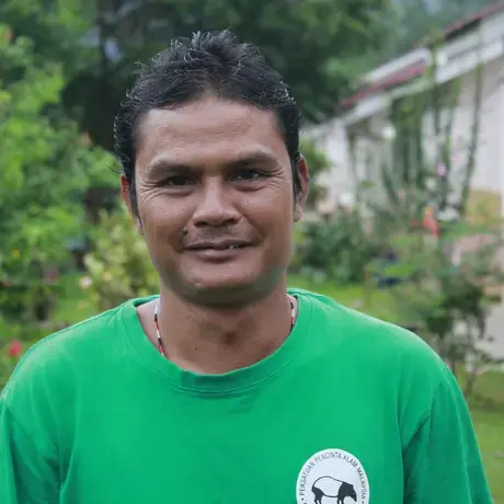Marisan A:K Pandak_TFR070.JPG Image of a person wearing a green shirt. A house and tropical forest is in the background.
