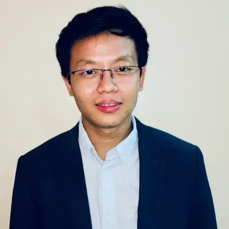 A person with a black jacket, light blue shirt, and glasses.