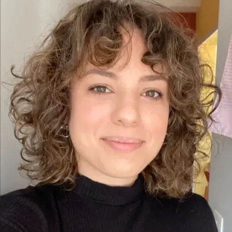 A woman with curly hair and brown eyes stares into the lens