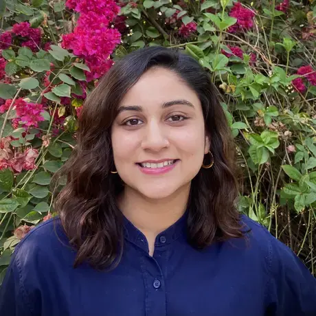 Headshot of Sidrah Fatma Ahmed. She stands in front of a flowering bush.