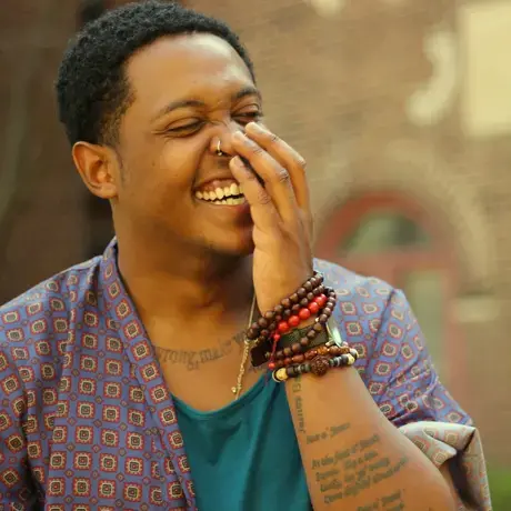 Photo of Danez Smith, partially covering their face while laughing.