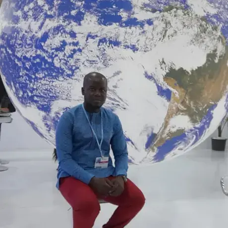A man sits atop a stool against a life-size, giant globe.