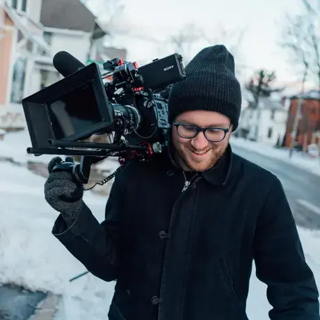 Will N. Miller walks down a snowy sidewalk with his video camera.
