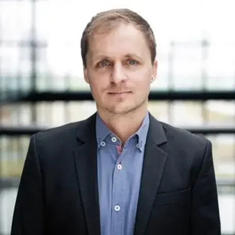 A man with short hair wearing a blue button down with a black blazer