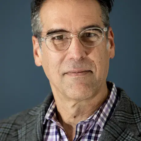 A man with short hair, glasses, wearing a plaid button down under a blazer