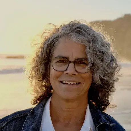 A woman with curly grey hair and glasses on a beach