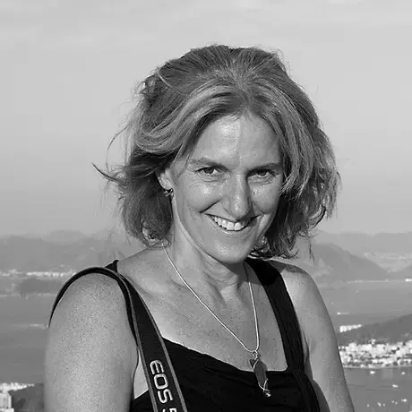 Black and white photo of a woman with shoulder-length hair wearing a black top with a camera strap around her shoulder