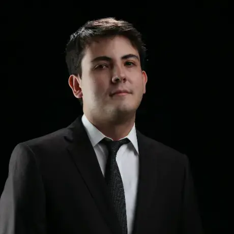 Headshot of a man wearing black suit jacket, white button down, and a black tie