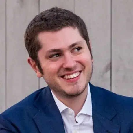 A man with short hair wearing a white button down and blue blazer