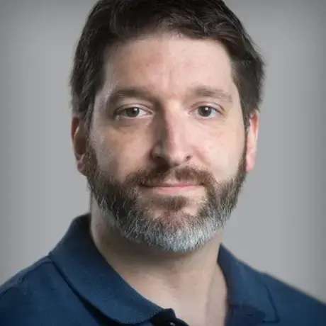 Headshot of a man with short dark hair wearing a navy button-down