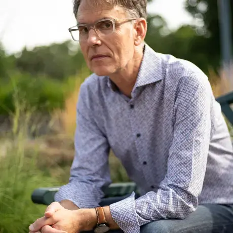 Todd sits on a bench wearing a patterned button down