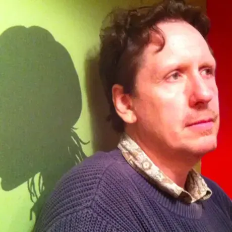 Trey wearing a blue sweater stands against a wall surrounded by green and red lighting