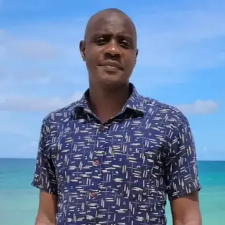Image of Adrams wearing a blue printed button-down with the ocean in the background