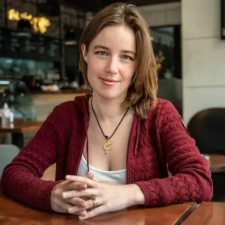 Aisha sits at a table wearing a red cardigan