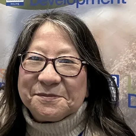 Linda Matsumoto is an Asian woman with black and gray hair and glasses. She is smiling into the camera.