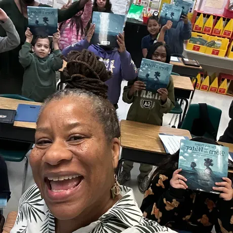 Project Lead, Veronica Jones, takes a selfie with students holding up copies of Born On The Water in the classroom