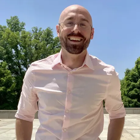 John Meehan smiles as he poses for a professional photo outdoors with trees in the background.