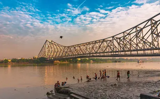 People bathe in the Ganges overlooking the Howrah Bridge in West Bengal. Image by ABIR ROY BARMAN / Shutterstock. India, 2019.