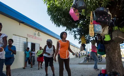 Workers retrieve lunch satchels left hanging in trees outside of a Sae-A Trading Company factory building at the Caracol Industrial Park in the north of Haiti on April 14. Sae-A is the anchor tenant of the $300 million-park, employing about 5,000 workers—still far short of the 60,000 jobs originally projected by 2017. The Clintons were instrumental at nearly every step in its creation. Image by Allison Shelley. Haiti, 2014.