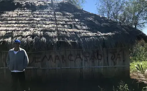 Cacique (or "Chief") Ezequiel João in front of the walls of his residence. "Demarcação Já!" (or "Demarcation Now!" is written as a form of protest to the government's long delay in demarcating and protecting the territories that were promised to his village. Image by Rafael Lima. Brazil, 2019.
