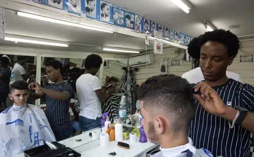 In this Wednesday, Aug. 8, 2018 photo, Eritrean migrant Gharmay Negassi works at a barbershop in Tel Aviv, Israel. African migrants coming into Israel have been detained, threatened with deportation, and faced hostility from lawmakers and residents. Now, they face another burden: a de facto 20 percent salary cut that has squeezed them financially and driven them further into poverty. Image by Caron Creighton. Israel, 2017.
