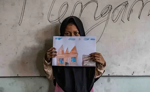 A 10-year old girl holds up her drawing of a home in a government run shelter. The girl is one of the surviving members of the families that carried out a string of ISIS-inspired suicide attacks in the city of Surabaya in May 2018. Image by Jurnasyanto Sukarno. Indonesia, 2018.