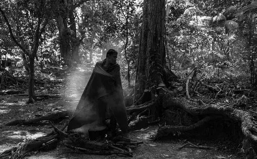 An indigenous man stands next to a tree and inhales medicinal gas.