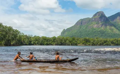 three children sitting in a canoe on a river with forest in the background