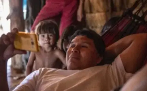 A man lying down and holds a phone with a child standing next to him.