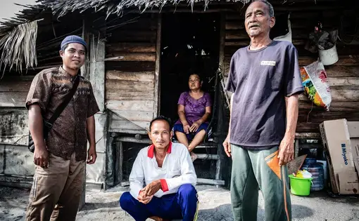 Three people look at the camera, in the foreground is a house.