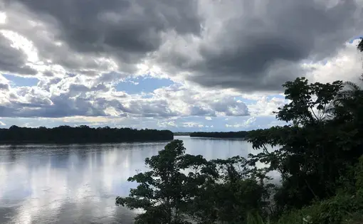 An aerial view of a lake surrounded by forest trees and clouds.