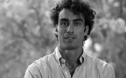 A man with curly hair and wears a white shirt smiles at the camera.