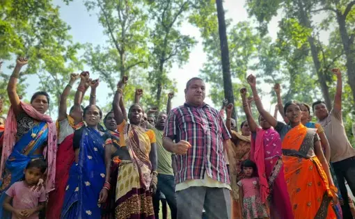 A crowd of eight to ten people raise their fists in the sky. In the foreground there is a forest.